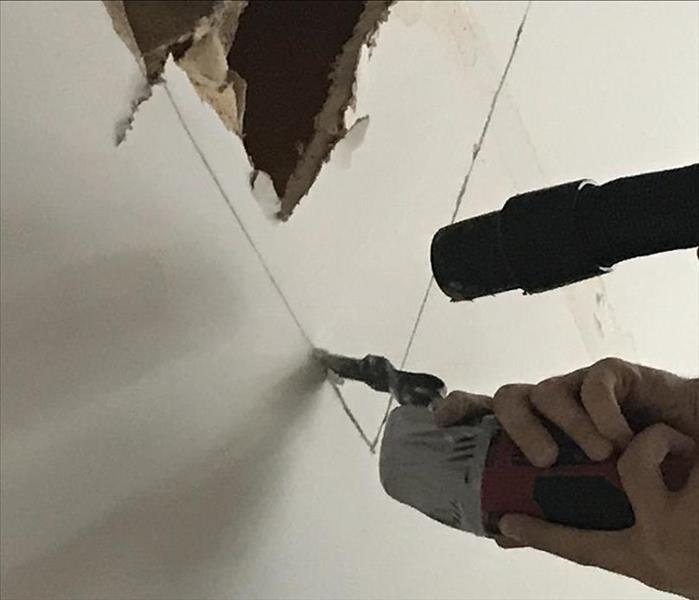 ceiling with jagged cut hole in drywall and technician hands with tools fixing the cuts