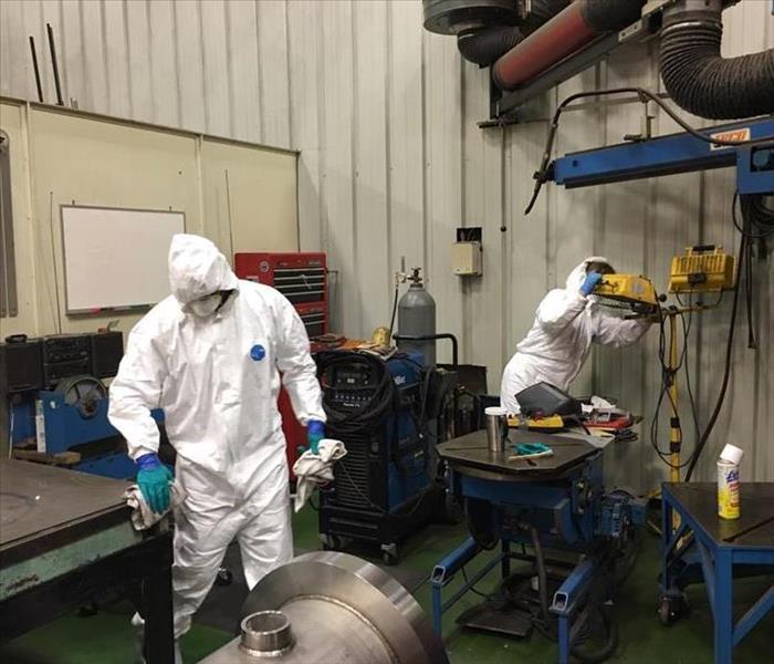 Two technicians in full PPE hand wiping industrial equipment  